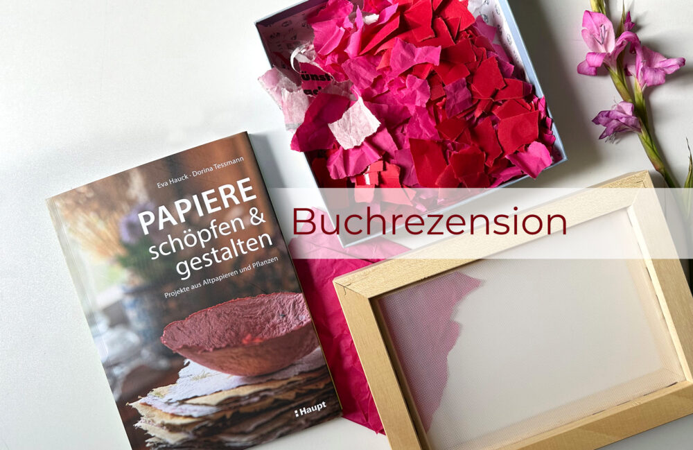 Das Buch "Papiere schöpfen und gestalten" liegt auf dem Tisch neben pinken Papierschnipseln, dem Schöpfrahmen und einer violetten Blüte. Darüber der Schriftzug "Buchrezension"